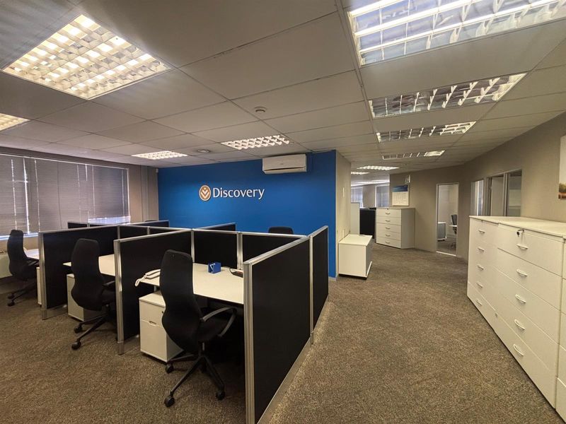 Open-plan office space featuring partitioned workstations, suspended ceilings with recessed lighting, wall-mounted air conditioning, and integrated storage cabinetry.