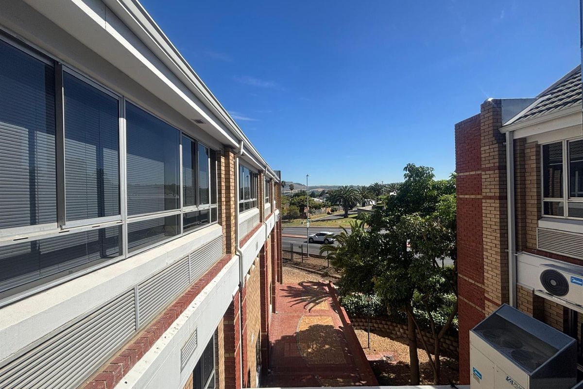 An elevated view of the office building exterior, featuring brick facade, aluminum windows, and external air conditioning units overlooking a paved courtyard and street.