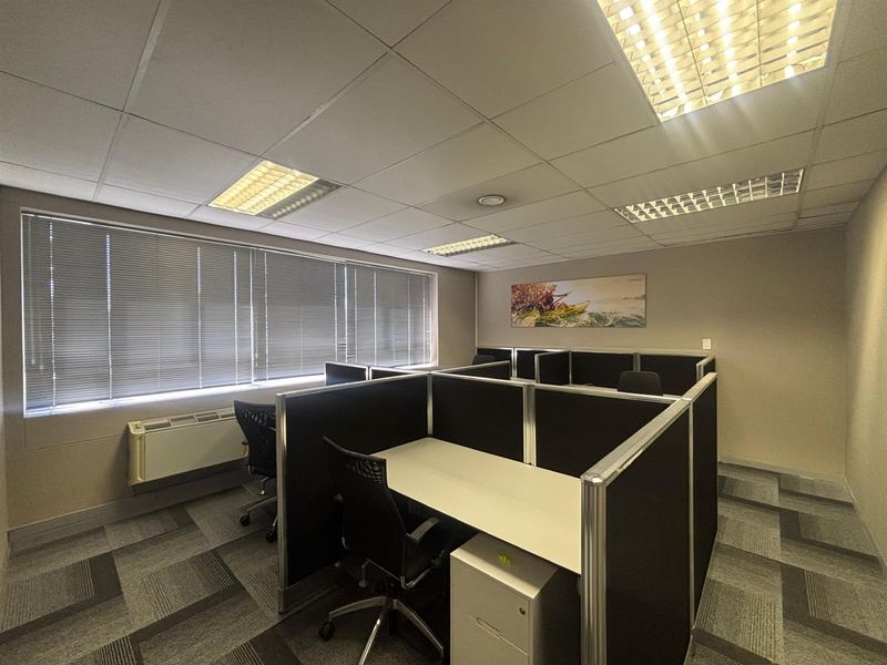 A functional office space featuring carpet tiles, suspended ceilings with recessed lighting, venetian blinds, and an integrated HVAC unit.