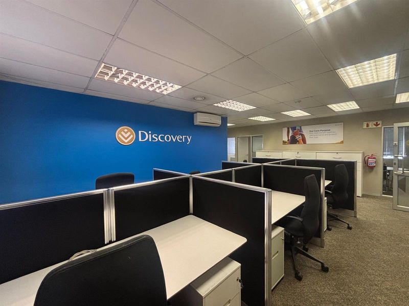 A professional office space featuring a suspended ceiling, recessed lighting, carpeted flooring, and integrated cubicle workstations with a branded feature wall.