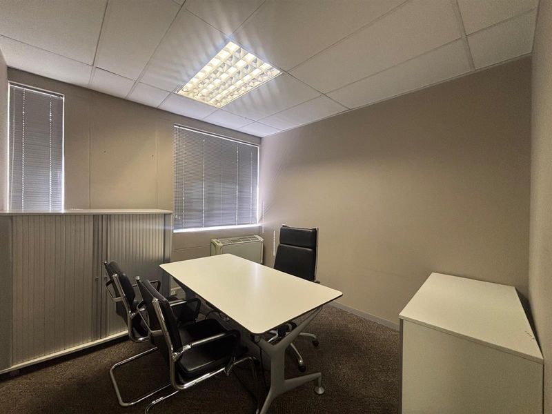 A functional office space featuring a suspended ceiling, recessed lighting, carpeted flooring, and window blinds, providing a professional environment for work.