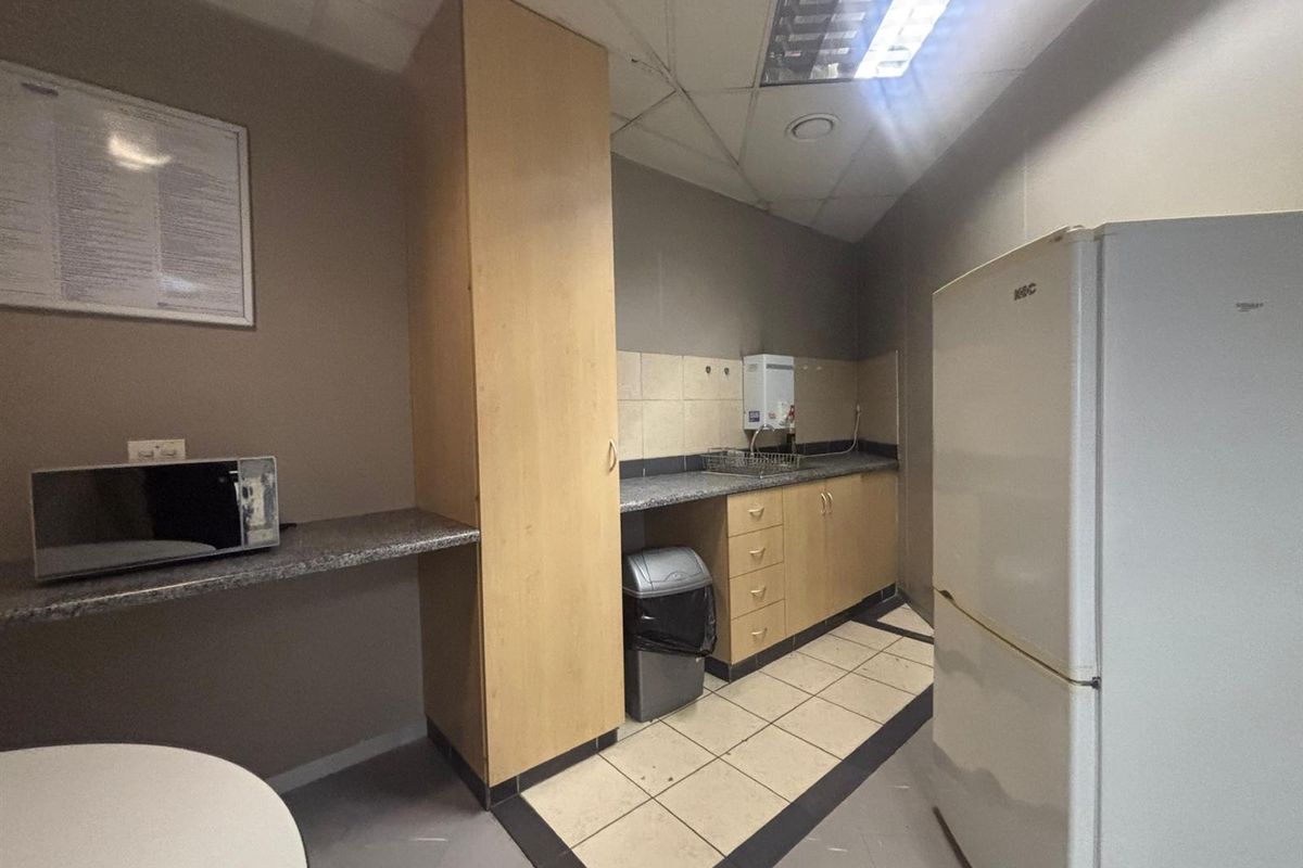 A functional office kitchenette featuring built-in cabinetry, granite countertops, and tiled flooring, providing a practical space for staff refreshments.