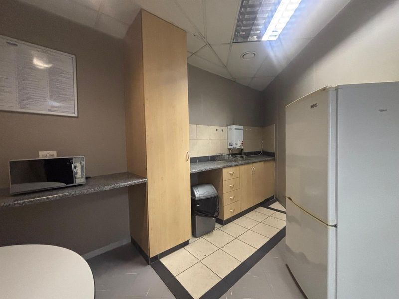 A functional office kitchenette featuring built-in cabinetry, granite countertops, and tiled flooring, providing a practical space for staff refreshments.