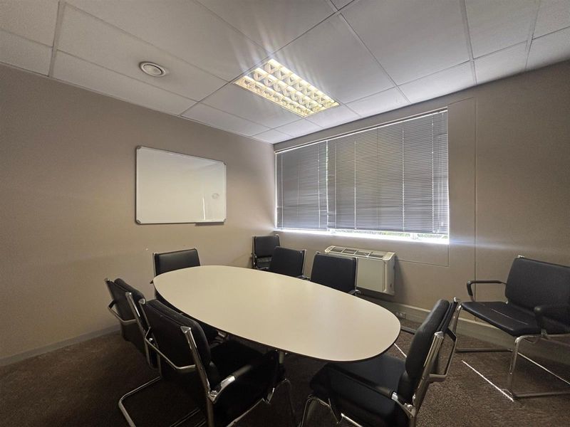 A functional office meeting room featuring a suspended ceiling, recessed lighting, wall-mounted whiteboard, and integrated HVAC unit with venetian blinds.