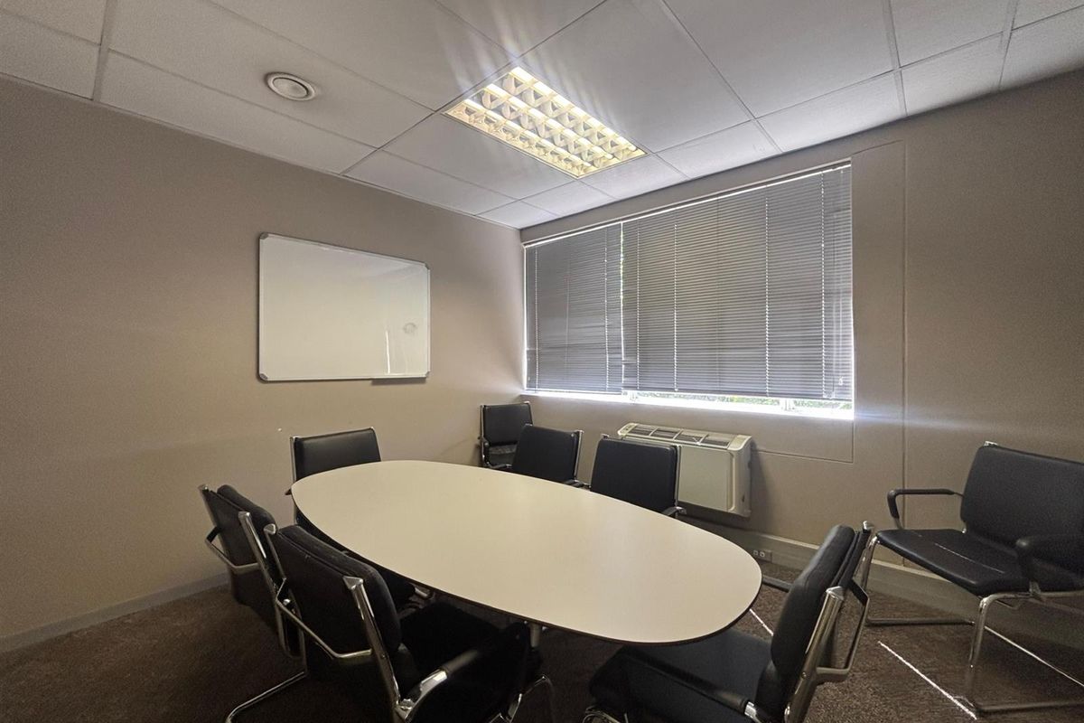 A functional office meeting room featuring a suspended ceiling, recessed lighting, wall-mounted whiteboard, and integrated HVAC unit with venetian blinds.