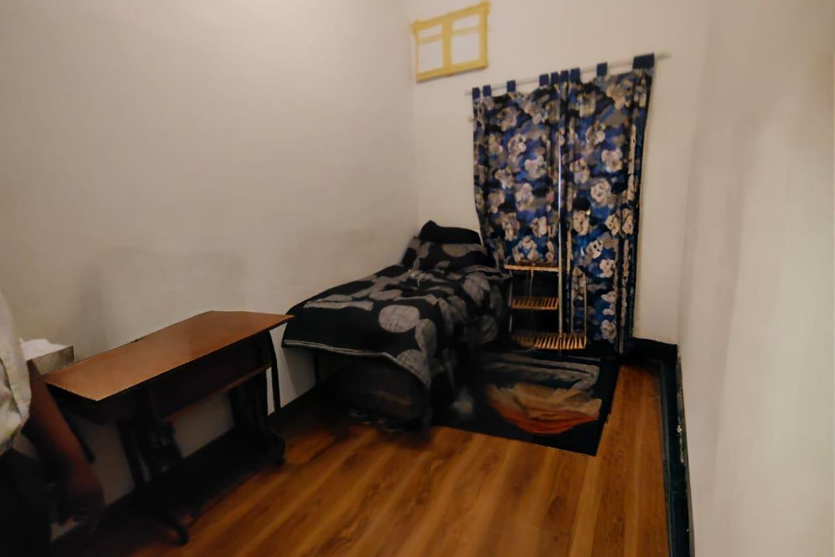 A compact bedroom featuring wood-look flooring and a window covered by patterned curtains.