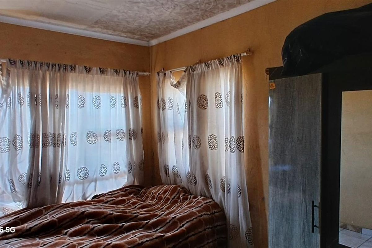 A bedroom featuring large windows with curtains and built-in wardrobe space, requiring cosmetic updates to the walls and ceiling.