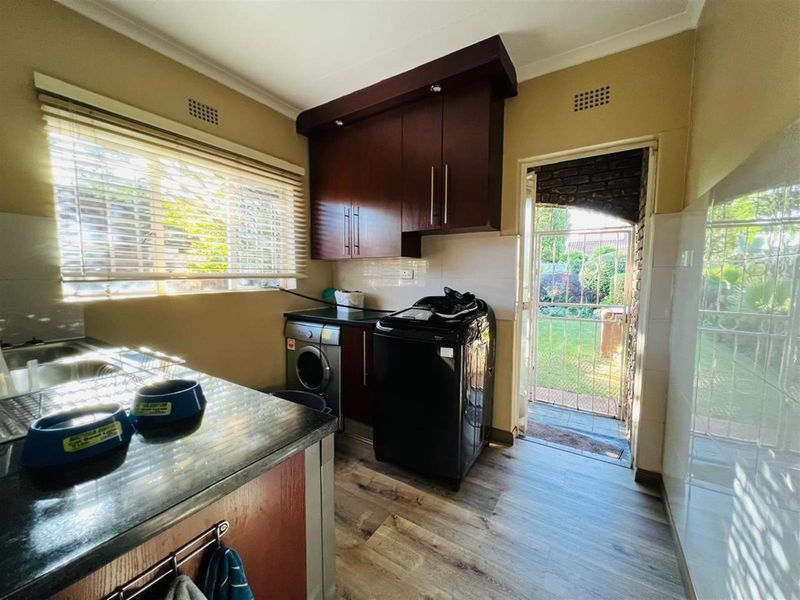 Functional laundry room featuring dark wood cabinetry, laminate flooring, and direct access to the rear garden area.