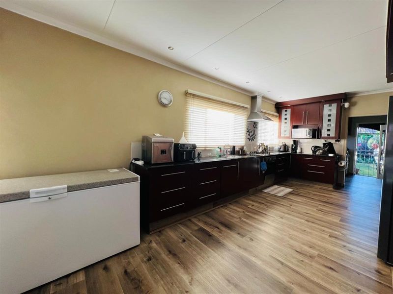 A functional kitchen featuring dark wood cabinetry, granite countertops, a stainless steel extractor fan, and wood-look laminate flooring.
