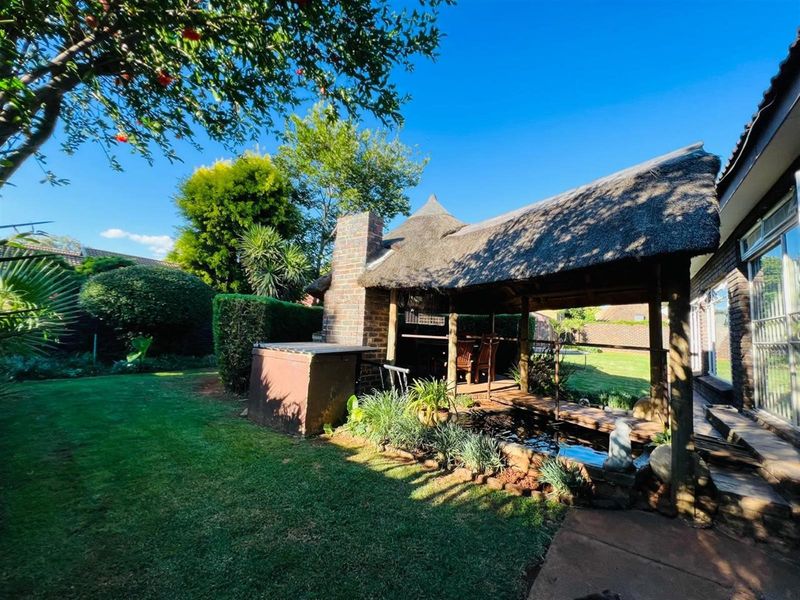 Outdoor entertainment area featuring a thatched lapa, built-in brick fireplace, and a small water feature set within a landscaped garden.