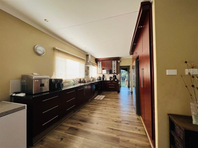 A galley-style kitchen featuring dark wood cabinetry, stone countertops, integrated appliances, and wood-look flooring with recessed ceiling lighting.
