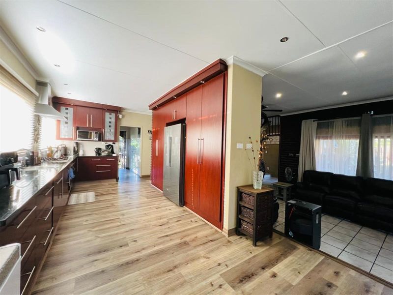 Open plan kitchen featuring dark wood cabinetry, integrated appliances, and wood-look flooring, seamlessly flowing into the adjacent living area.