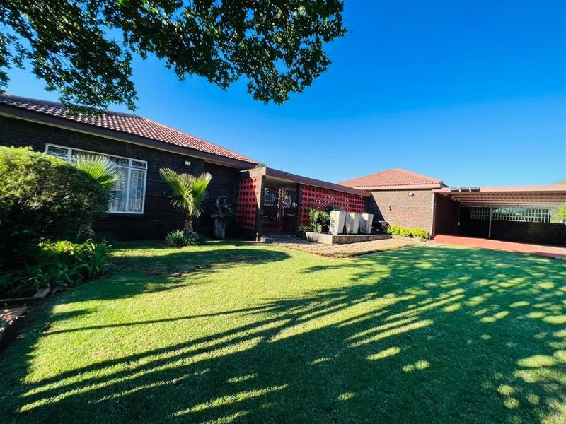 A view of the property's front exterior, featuring a brick facade, tiled roof, landscaped lawn, and a covered carport area.