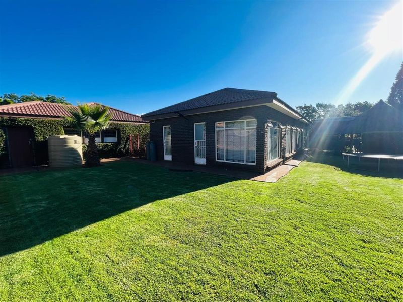 Rear view of the house featuring dark brick exterior, tiled roof, and a well-maintained lawn area.