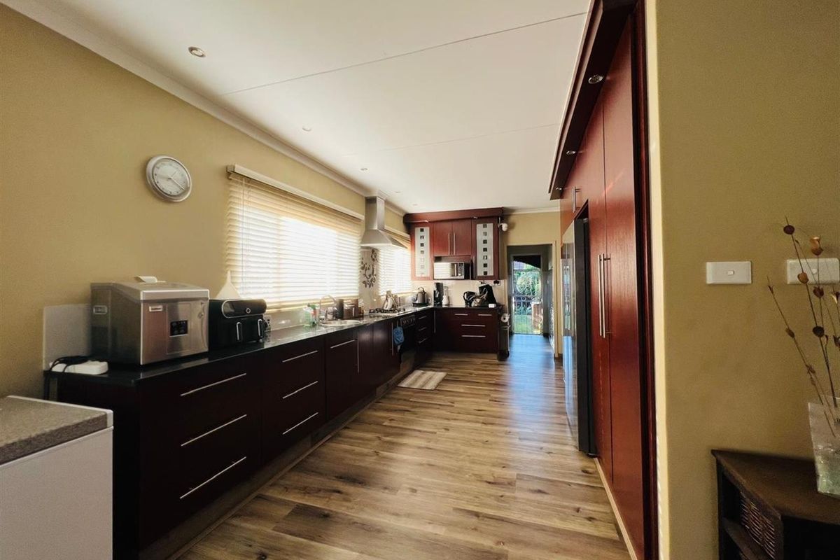 A galley-style kitchen featuring dark wood cabinetry, stone countertops, integrated appliances, and wood-look flooring with recessed ceiling lighting.
