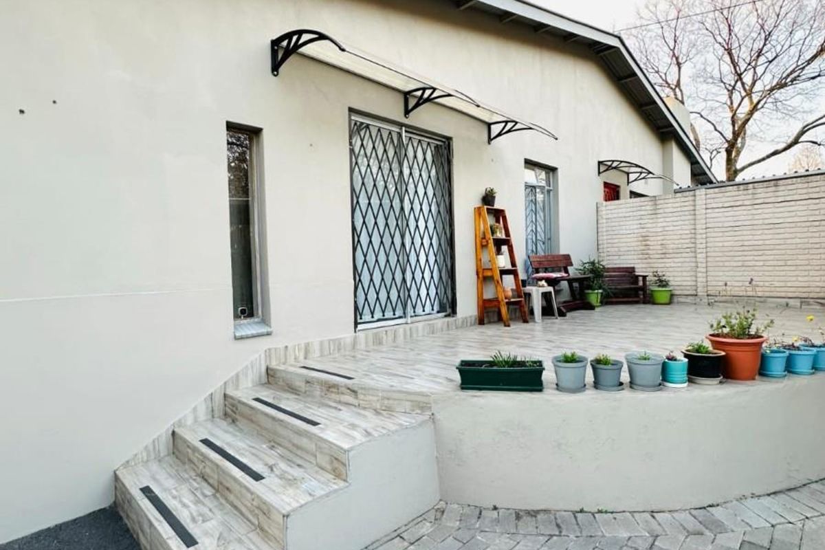 A rear exterior view featuring a raised tiled patio, security gates, and a paved area, providing a functional outdoor space.
