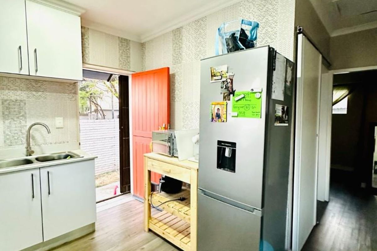 A functional kitchen area featuring white cabinetry, a stainless steel sink, and wood-look laminate flooring with direct access to an outdoor space.
