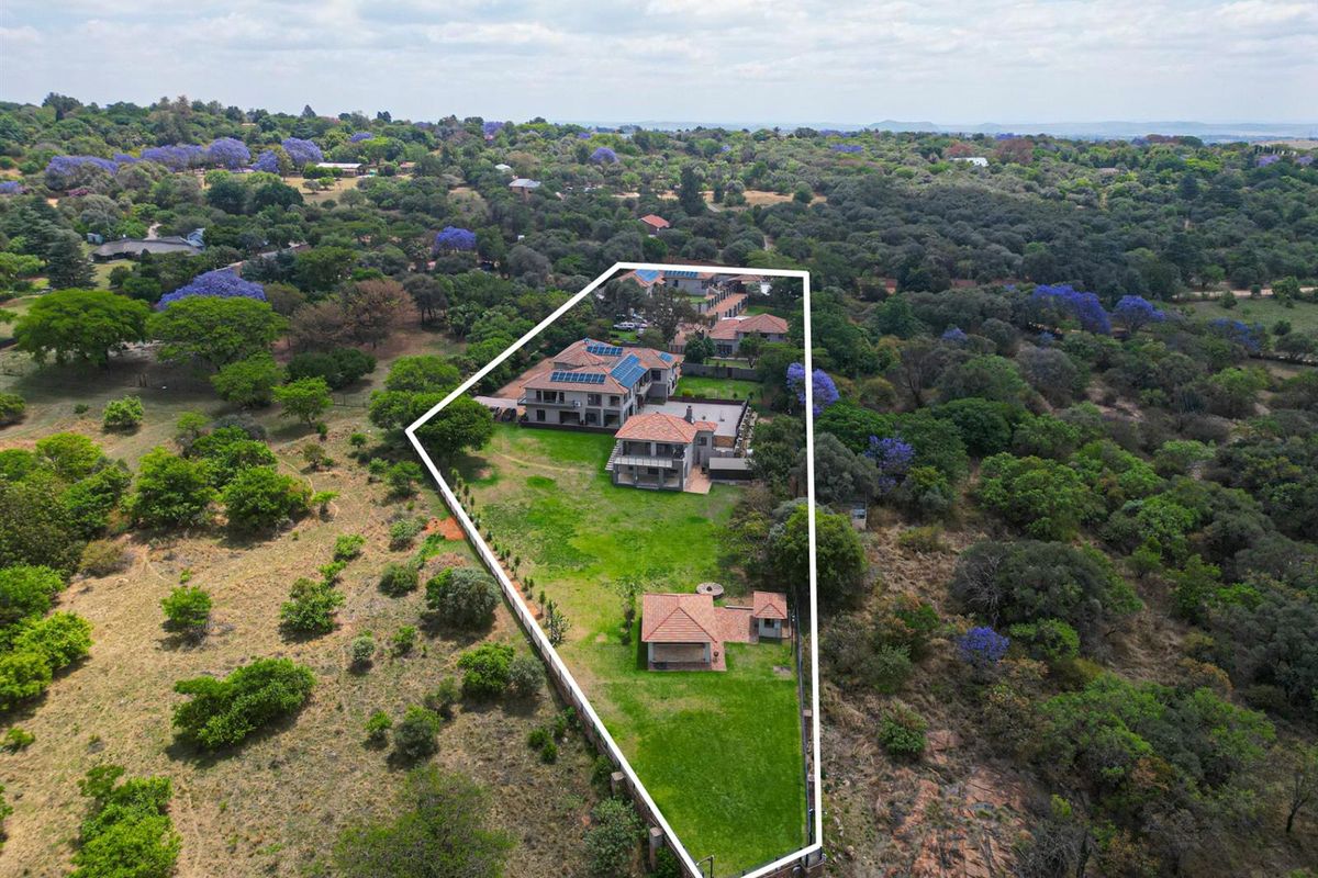 Aerial view of a large residential property featuring multiple buildings, expansive landscaped grounds, and solar panels, set within a lush, wooded estate environment.