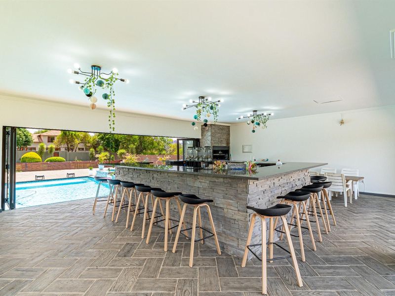 Spacious indoor entertainment area featuring a large stone-clad bar, built-in braai, and seamless flow to the outdoor pool area through folding doors.