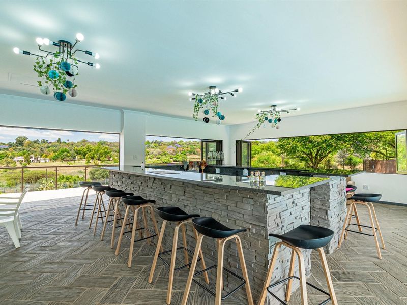 Spacious open-plan entertainment area featuring a large stone-clad bar counter, modern lighting, and expansive folding doors opening to scenic landscape views.