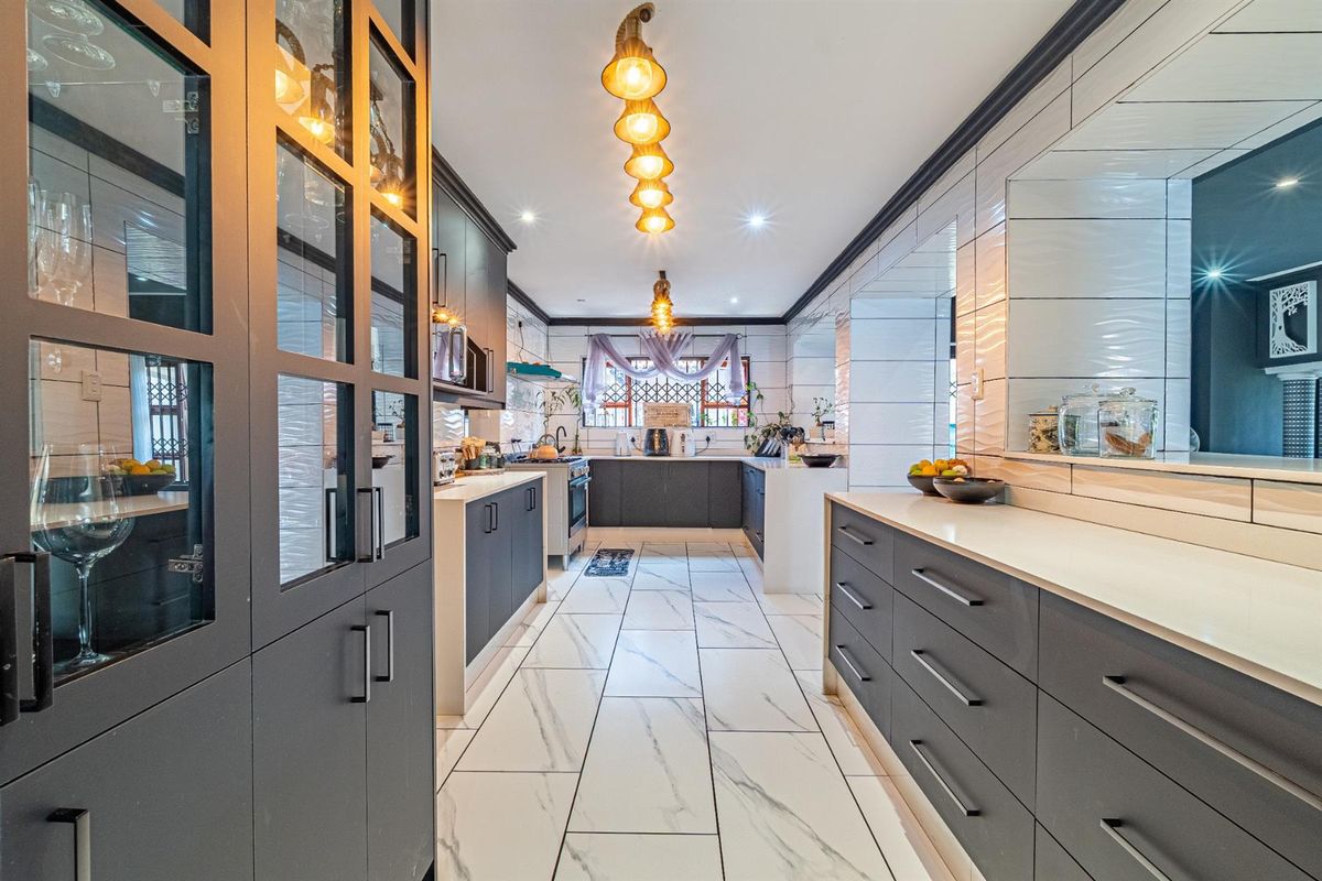 Modern kitchen featuring dark cabinetry, white stone countertops, marble-look floor tiles, and integrated lighting, offering a sleek and functional culinary space.