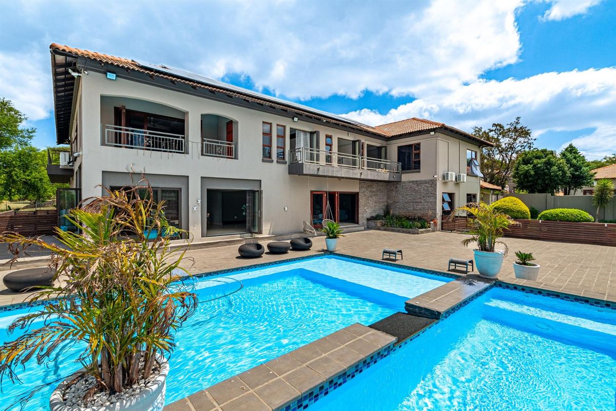 A spacious rear exterior view featuring a large swimming pool, paved patio area, and a two-story residence with balconies and tiled roofing.