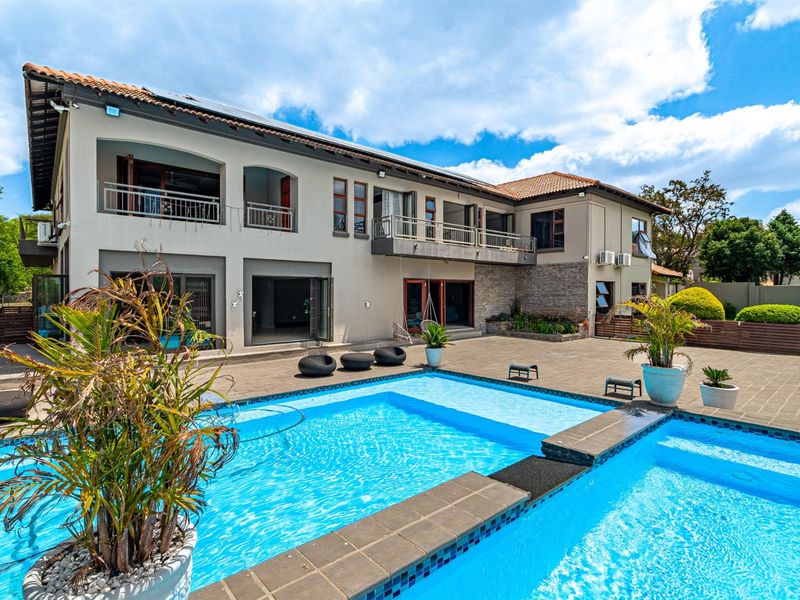 A spacious rear exterior view featuring a large swimming pool, paved patio area, and a two-story residence with balconies and tiled roofing.