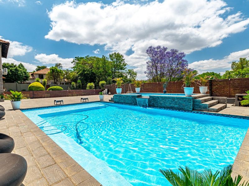 A well-maintained swimming pool area featuring a stone-clad water feature, paved surround, and timber perimeter fencing.