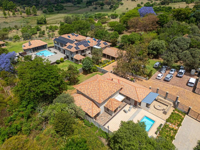 Aerial view of the property showcasing multiple buildings, two swimming pools, solar panel installations, and extensive landscaped grounds with mature trees.