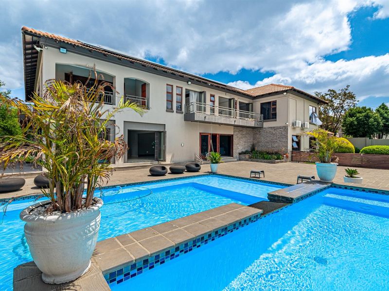 Spacious rear exterior view featuring a large swimming pool, paved patio area, and a multi-level house with balconies and sliding glass doors.