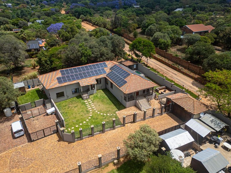 Aerial view of a residential property featuring a tiled roof with solar panels, a landscaped garden, paved driveway, and secure perimeter fencing.
