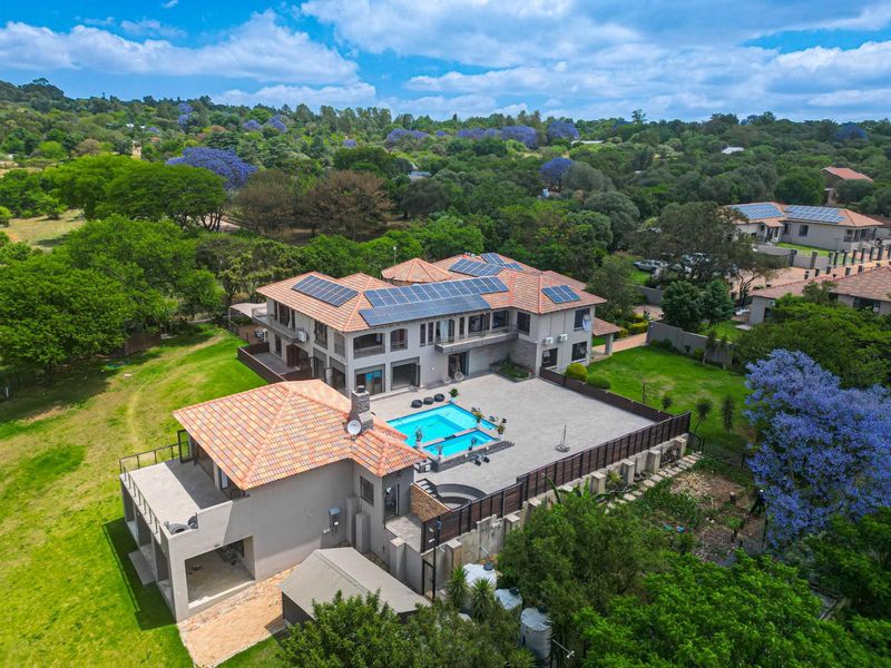 Aerial view of a large residential property featuring a tiled roof, solar panels, a swimming pool, and expansive landscaped grounds.
