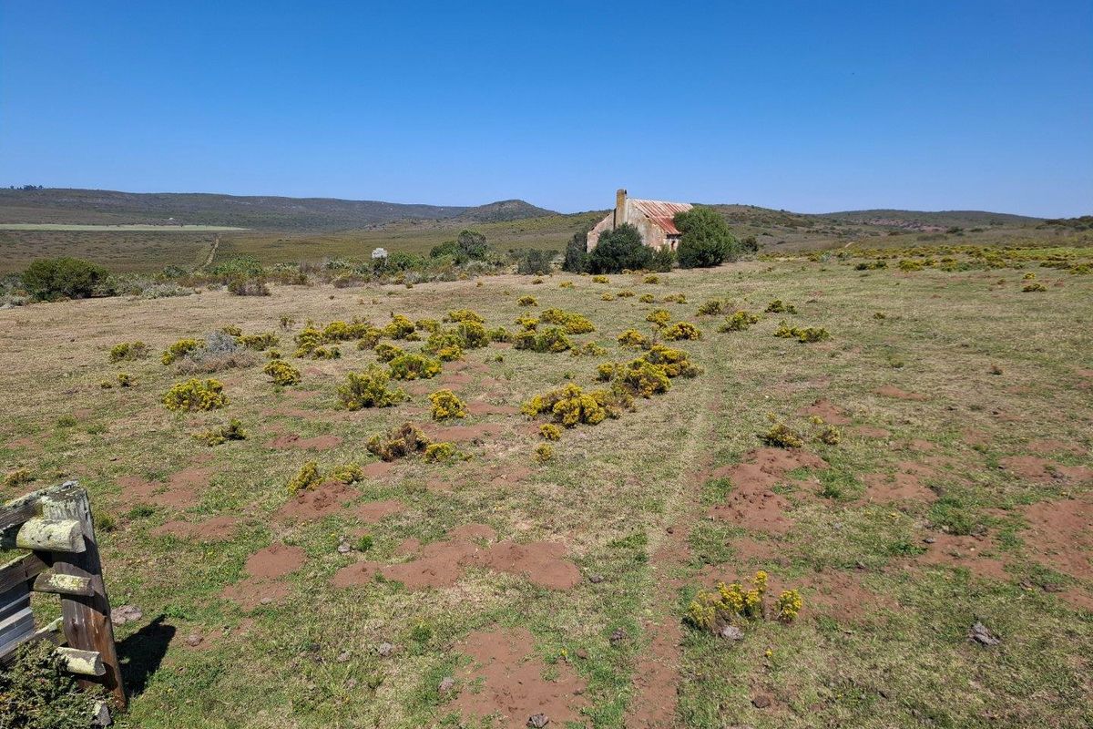 A remote farm property featuring a small, weathered structure set within a vast, open landscape with rolling hills in the distance.