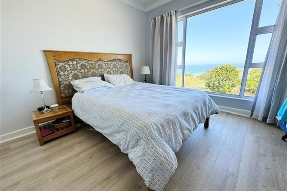 A bright bedroom featuring light wood-look flooring, crown molding, and a large window offering expansive ocean views.