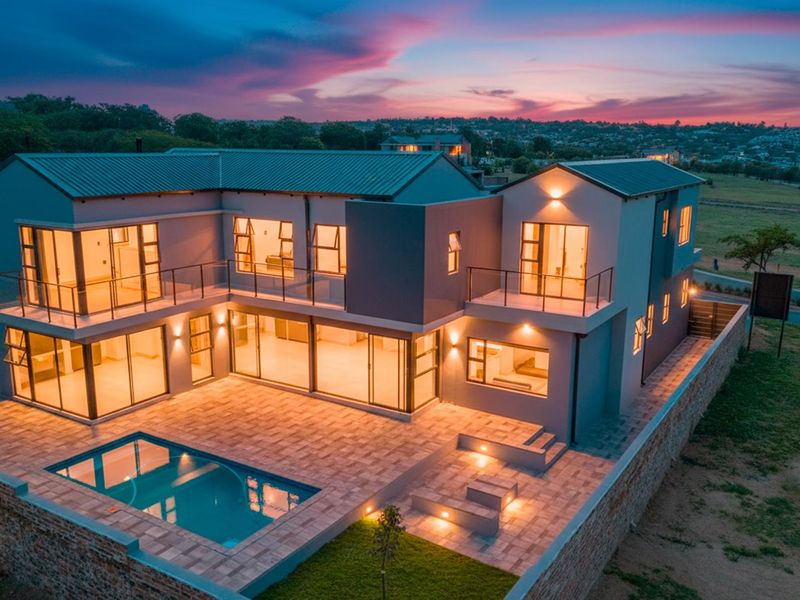 Aerial view of a modern two-story residence featuring a swimming pool, paved patio area, and multiple balconies at dusk.