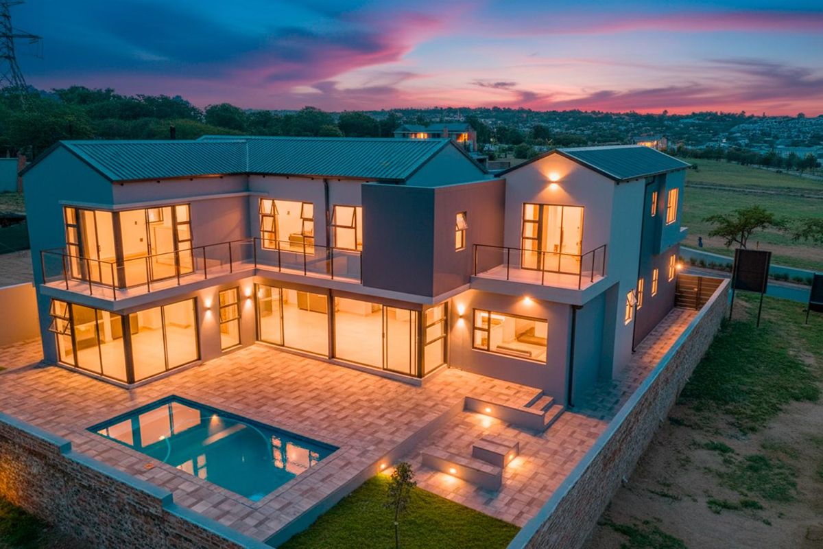 Aerial view of a modern two-story residence featuring a swimming pool, paved patio area, and multiple balconies at dusk.