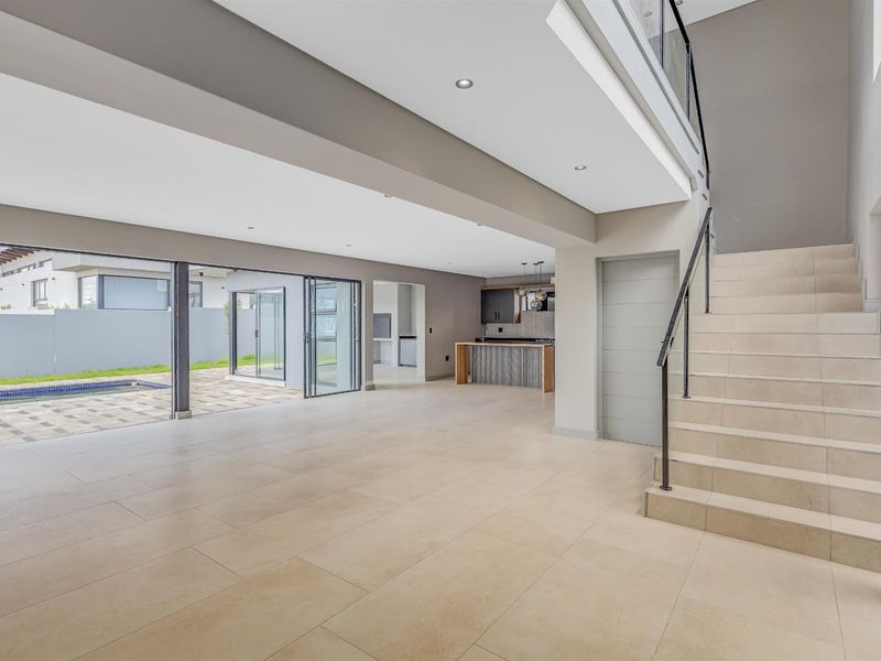 Spacious open-plan living area featuring large sliding glass doors leading to the patio and pool, complemented by a modern staircase and kitchen.