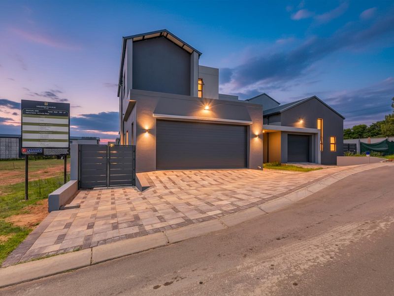 Modern double-story residential property featuring a paved driveway, dual automated garages, and contemporary architectural design at dusk.