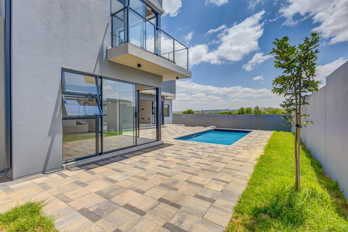 Rear view of the property featuring a paved patio, a swimming pool, and a balcony with glass balustrades.
