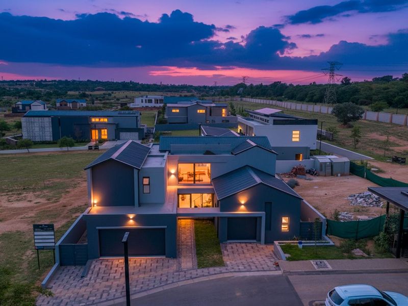 Aerial view of a modern double-story residential house at dusk, featuring a paved driveway, double garage, and contemporary architectural design.