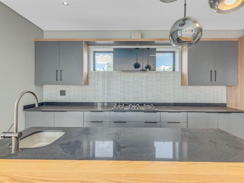 Modern kitchen featuring sleek grey cabinetry, stone countertops, a built-in gas hob, extractor fan, and a central island with a prep sink.