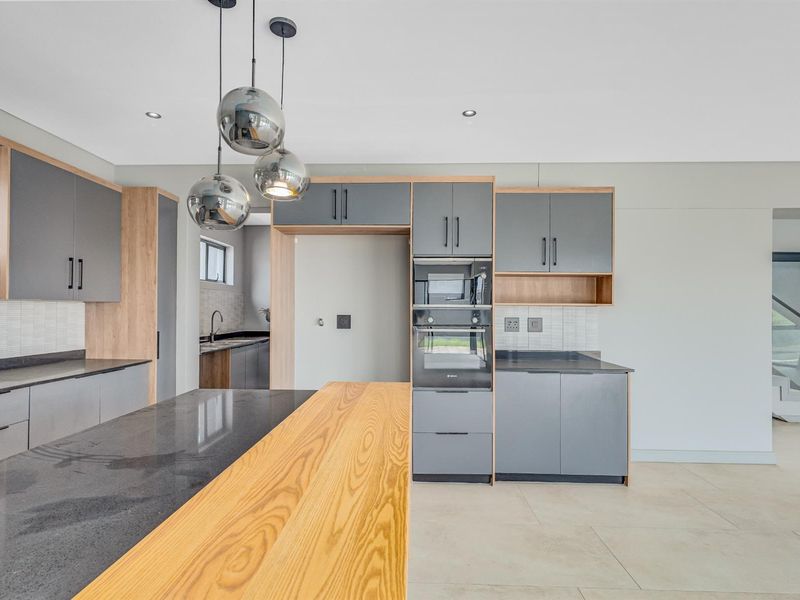 Modern kitchen featuring two-tone cabinetry, stone countertops, integrated oven, and a breakfast bar, with an adjacent scullery area visible.