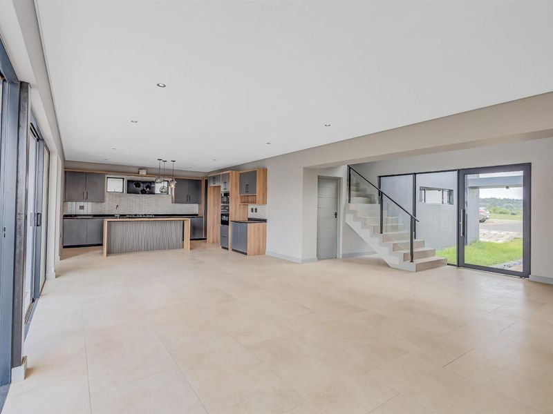 Spacious open-plan living area featuring a modern kitchen with built-in cabinetry, tiled flooring, and a staircase leading to the upper level.