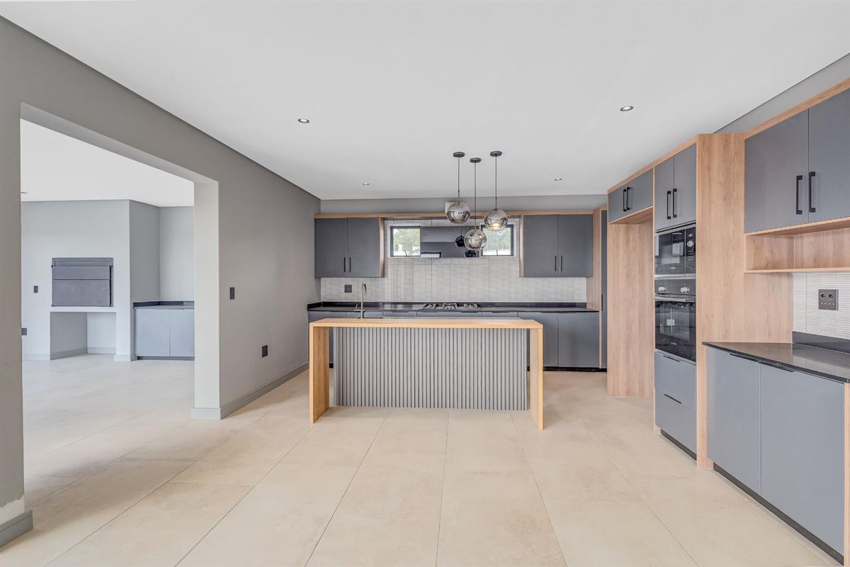 Modern open-plan kitchen featuring sleek grey cabinetry, wood-tone accents, integrated oven, and a central island, seamlessly flowing into an adjacent utility area.