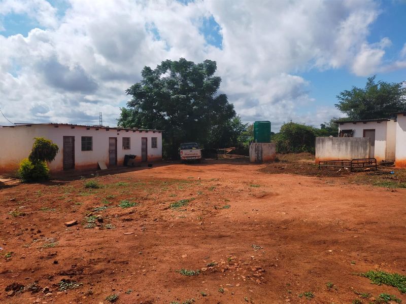 Rear exterior view of a commercial property featuring a large unpaved yard, a water storage tank, and basic single-story building structures.