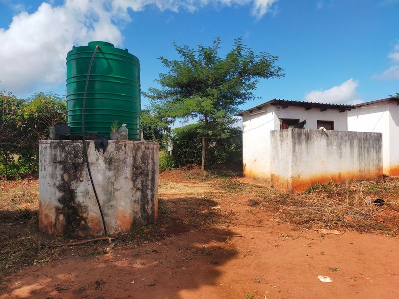 Exterior view of a commercial property featuring a water storage tank on a concrete stand and a small masonry outbuilding.