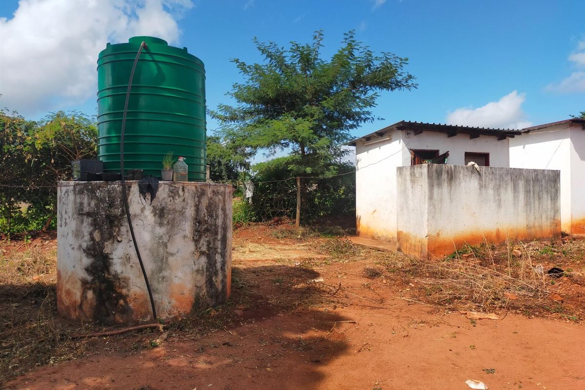 Exterior view of a commercial property featuring a water storage tank on a concrete stand and a small masonry outbuilding.