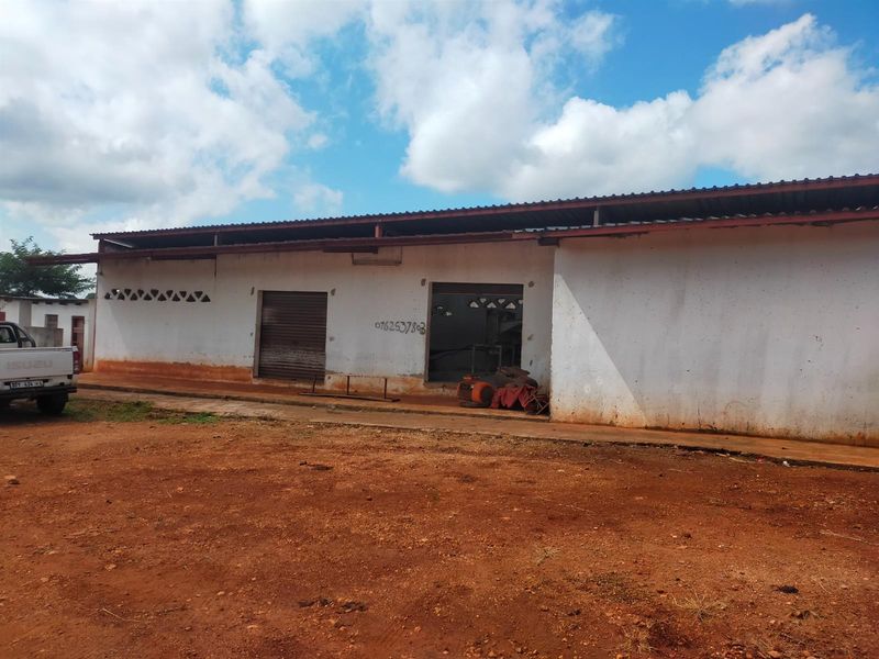 Front exterior view of a commercial building featuring a corrugated metal roof, roller shutter door, and ventilation blocks, set on an unpaved lot.