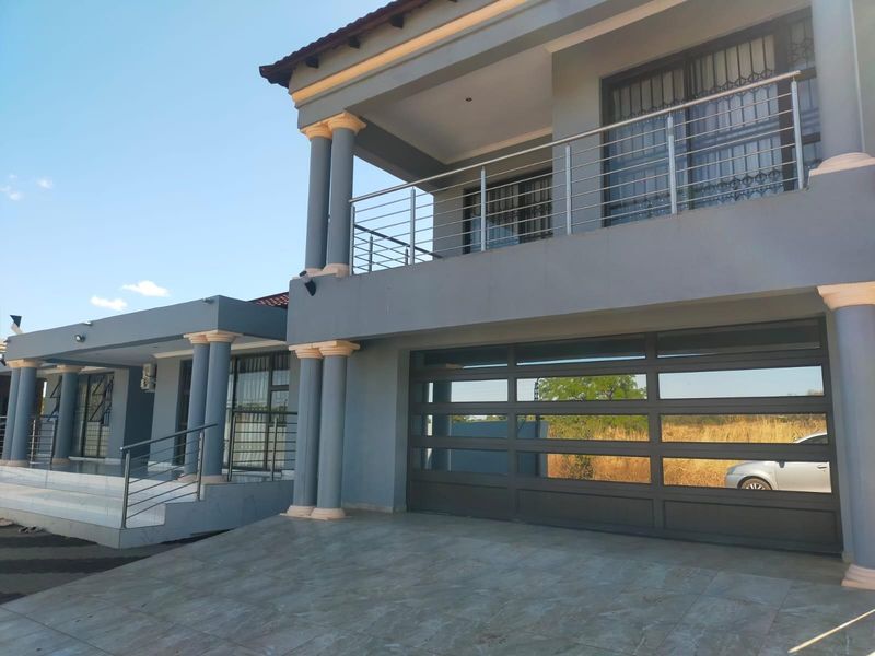 Modern double-story residential facade featuring a large garage, tiled driveway, and an upper-level balcony with stainless steel balustrades.