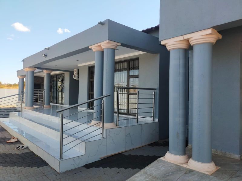 A spacious covered patio featuring tiled flooring, stainless steel balustrades, and decorative columns, providing a clean and modern outdoor entertainment area.